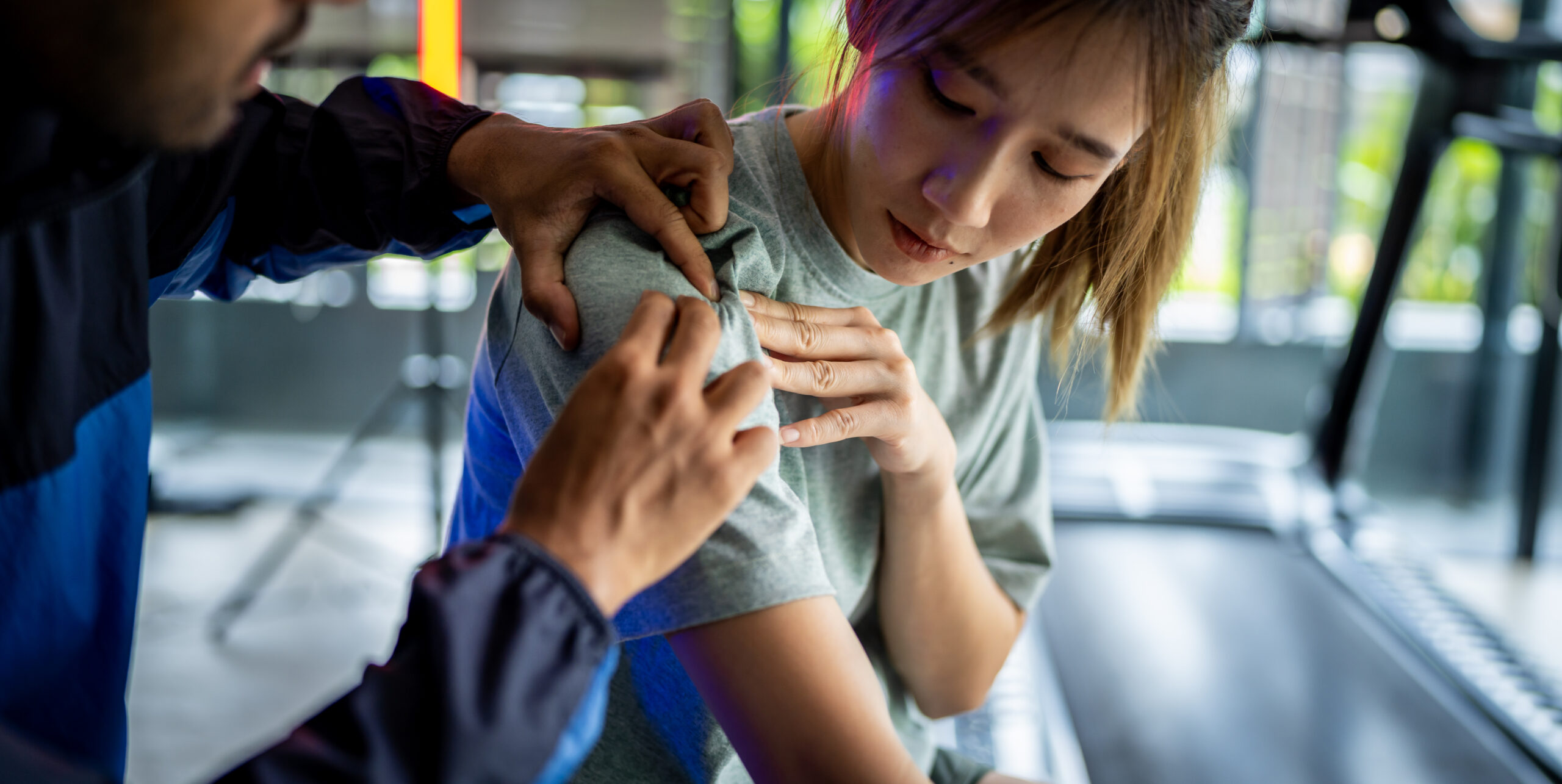 Trainer assisting a woman with shoulder injury during physical rehabilitation session at the gym 
