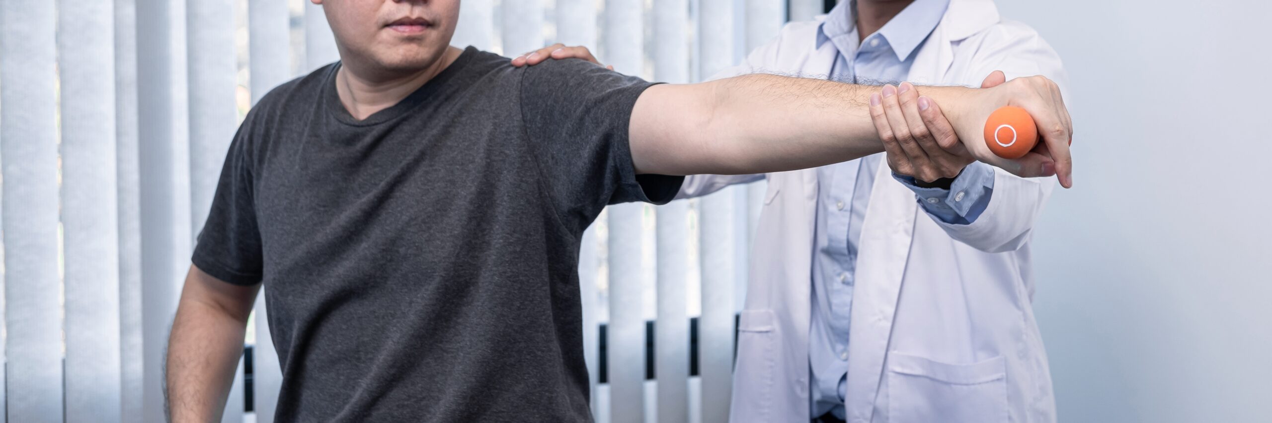 Physical therapist guiding a patient with a shoulder injury through a resistance exercise using an orange ball