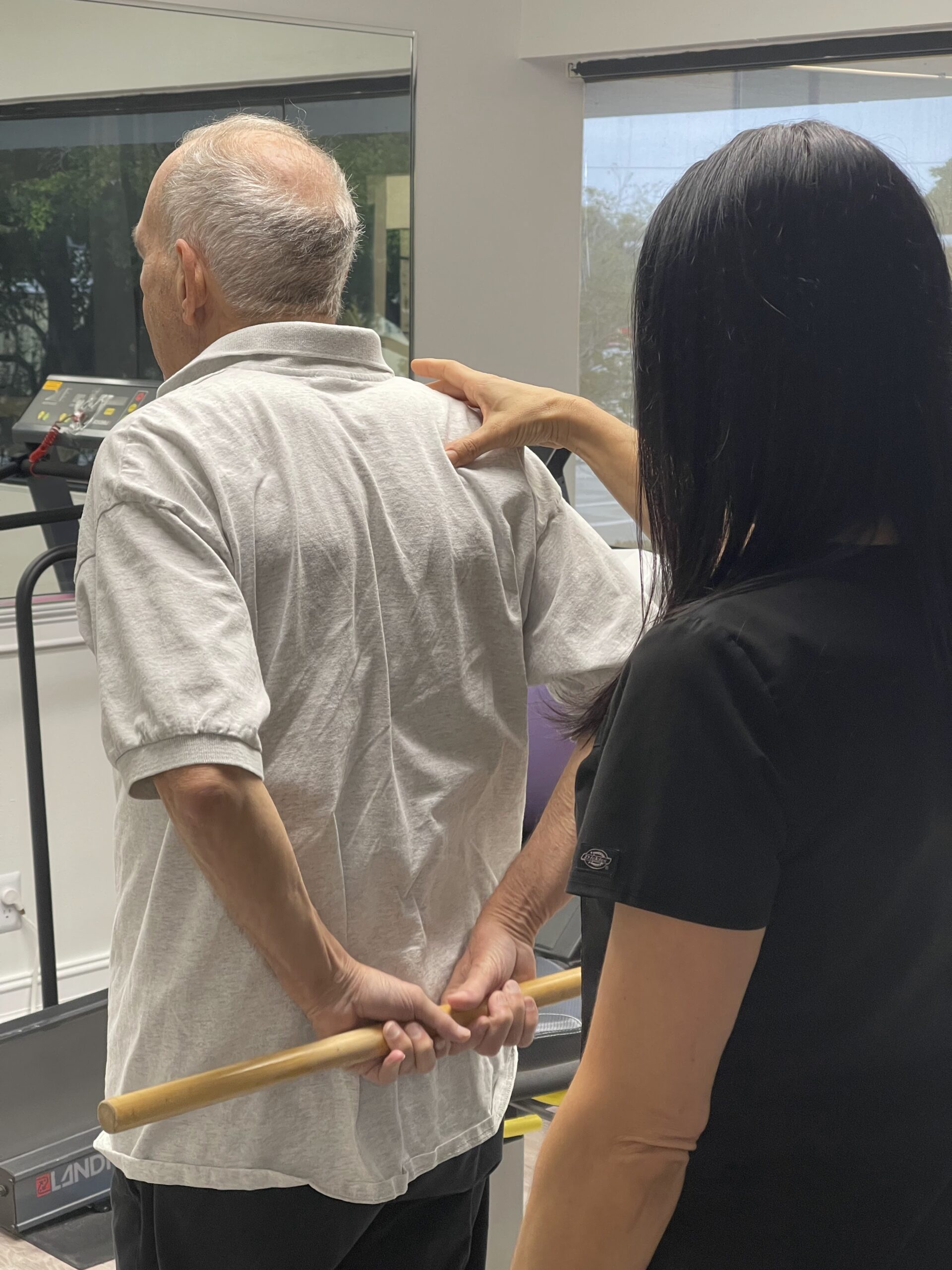 Physical therapy session in Deerfield Beach with therapist guiding senior patient through shoulder mobility exercise
