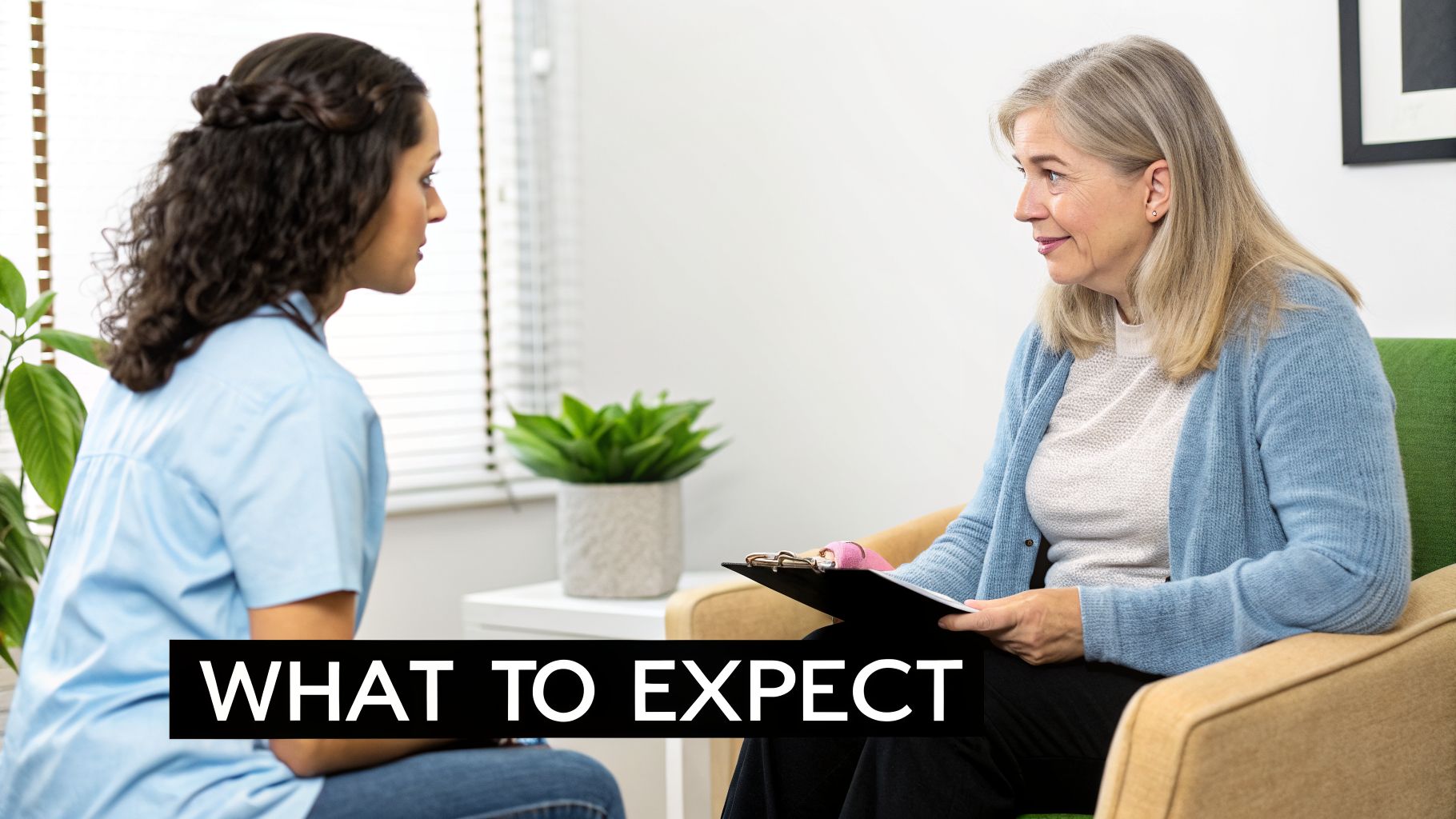 Two women, likely a therapist and patient, discussing in a bright, modern office with a plant.