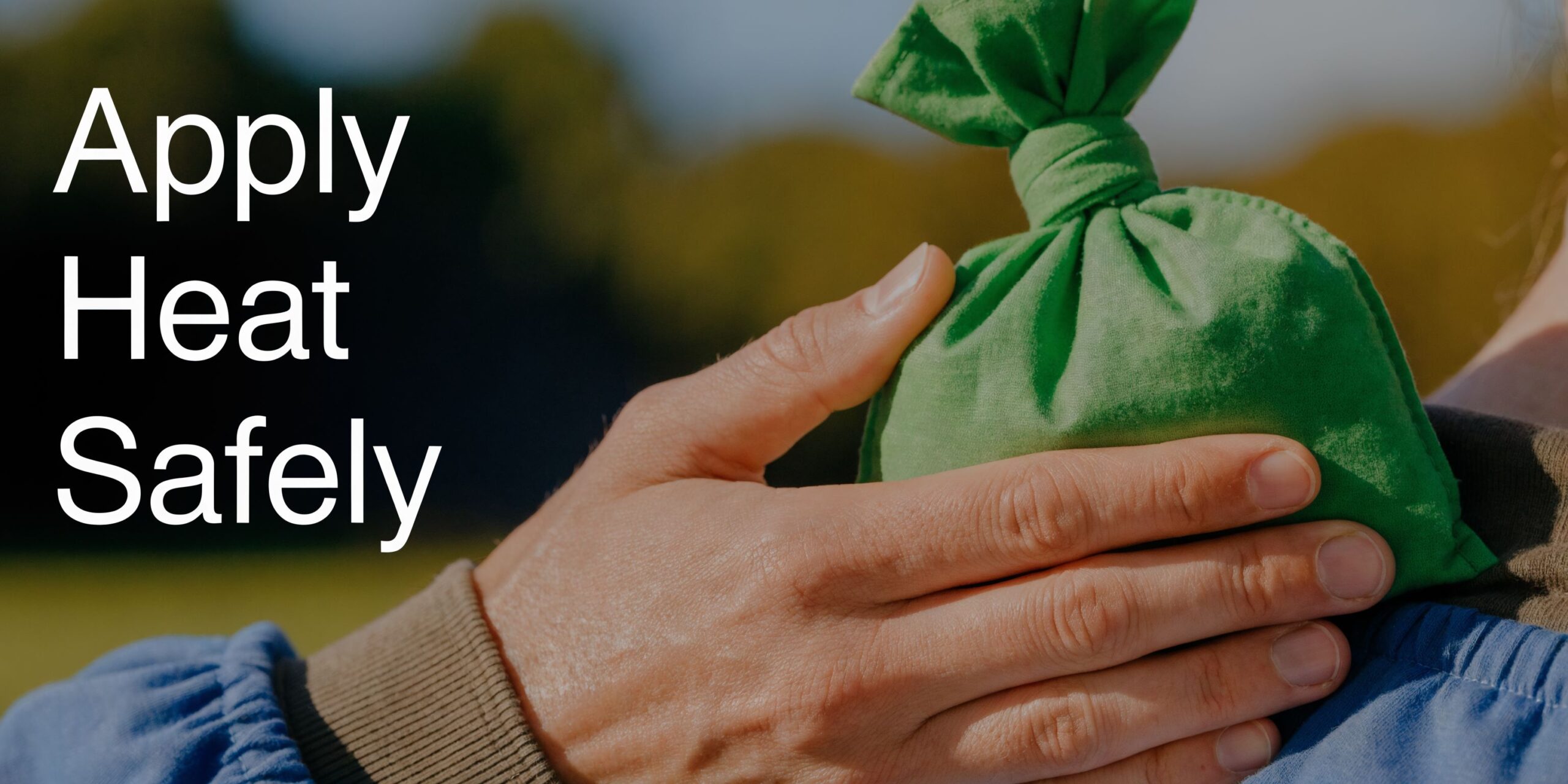 A close-up of a person's hand holding a green fabric heat pack against their shoulder area.