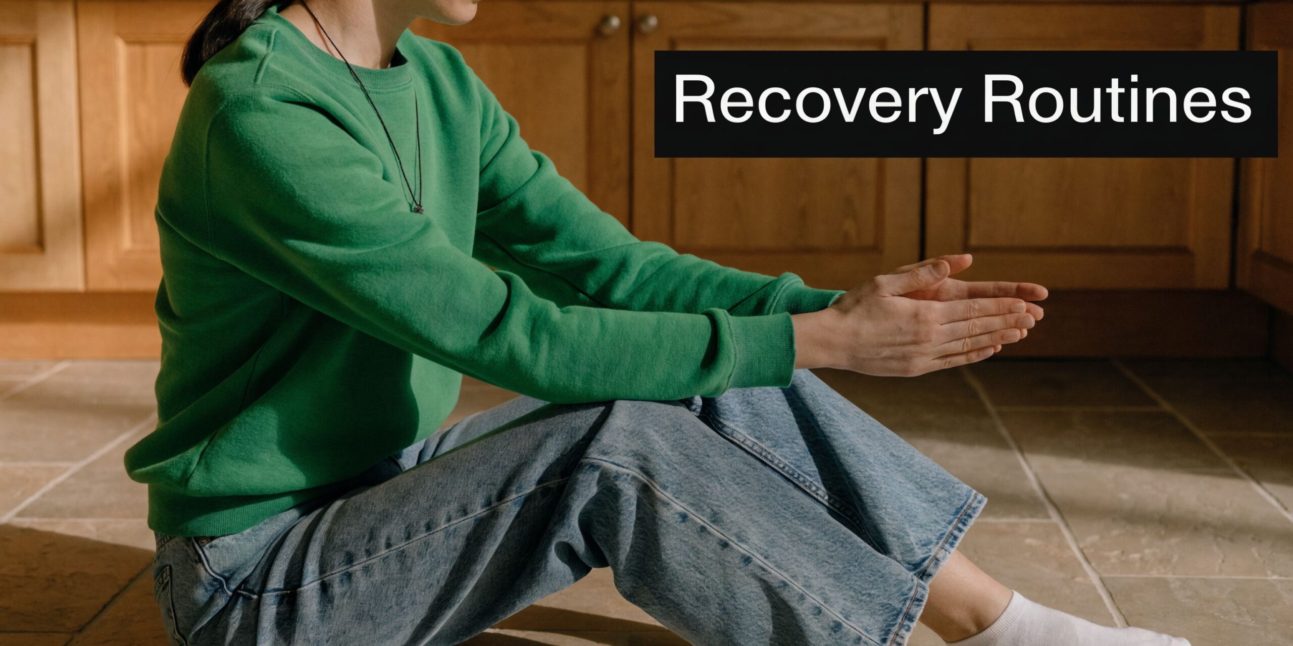 A person sitting on the kitchen floor practicing recovery routines, focused on mindful movement and healing.