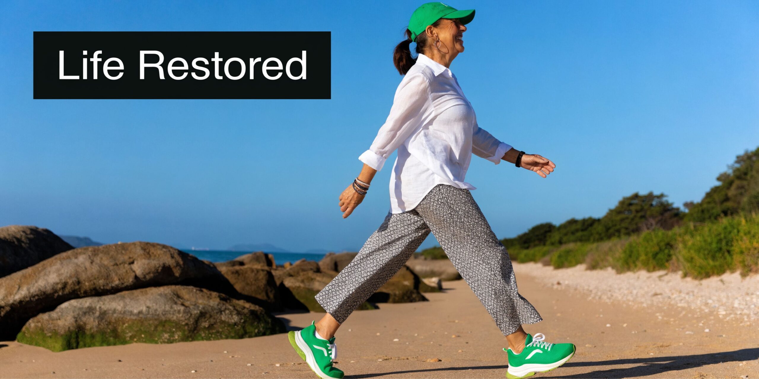 A happy senior woman walking on the beach in comfortable clothing and green sneakers for health.
