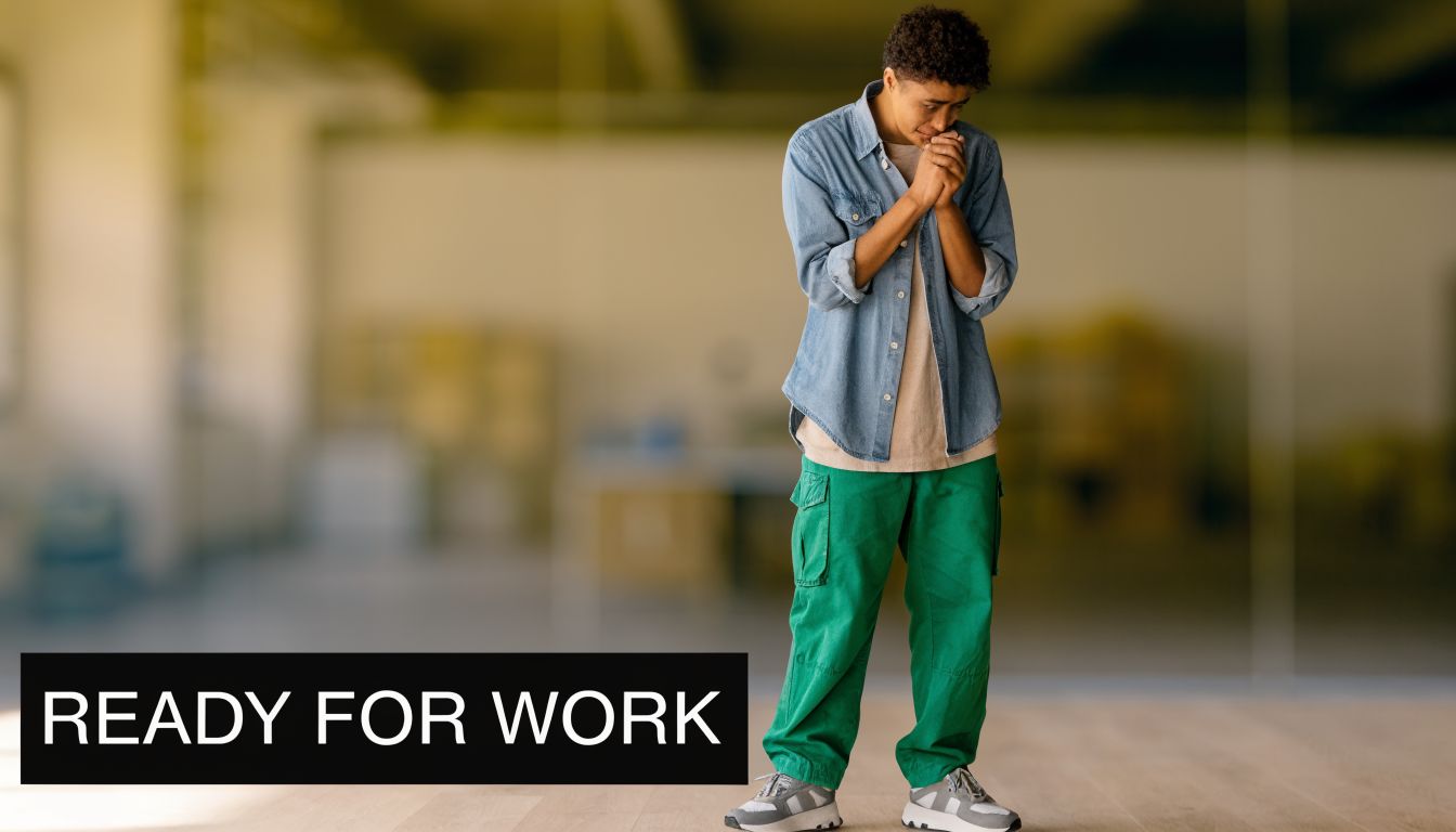 A young person standing with hands clasped together, looking thoughtful in a professional or office-like environment.