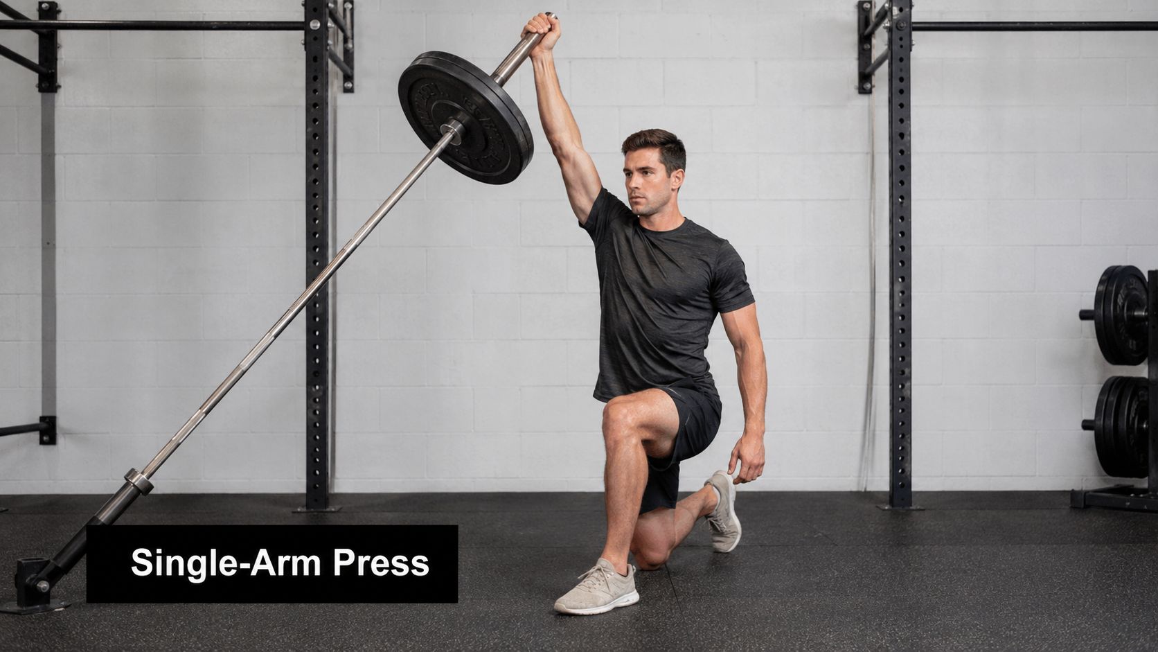 A fit man performing a single-arm landmine press while kneeling on the gym floor for shoulder stability.
