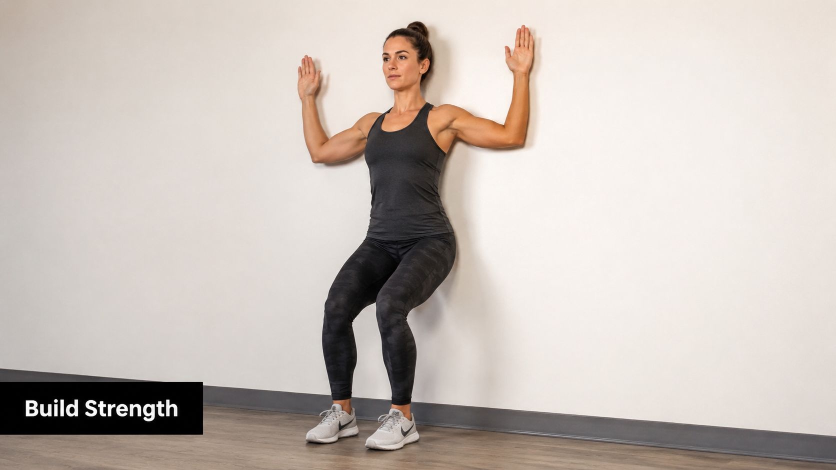 A woman performing a wall slide exercise against a plain wall to build upper body strength.