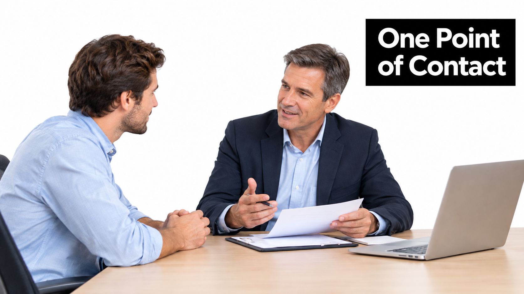 A professional manager in a suit discussing documents with a young employee at an office desk.
